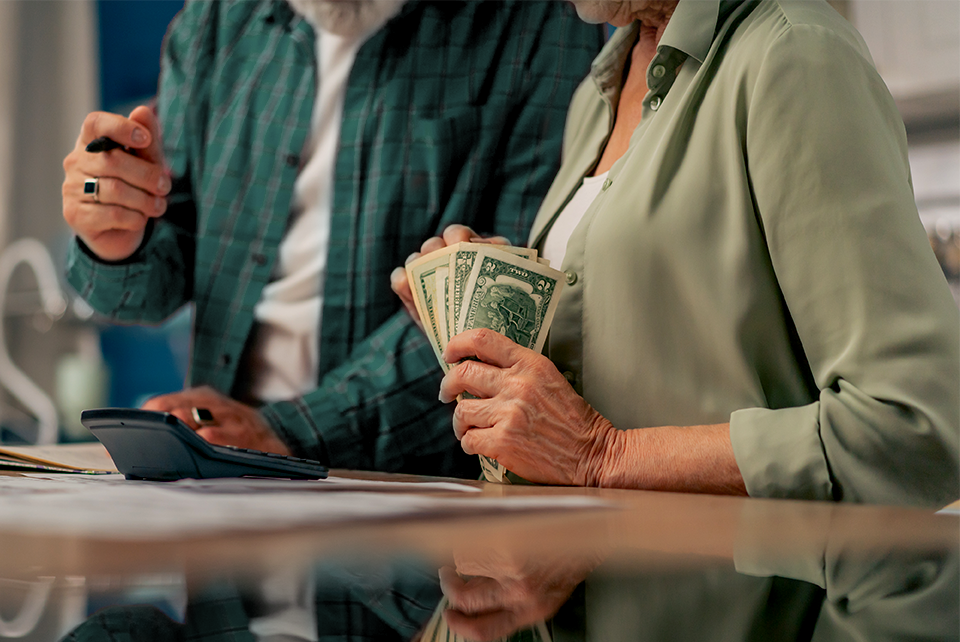 An older couple at their kitchen table counting cash beside a calculator